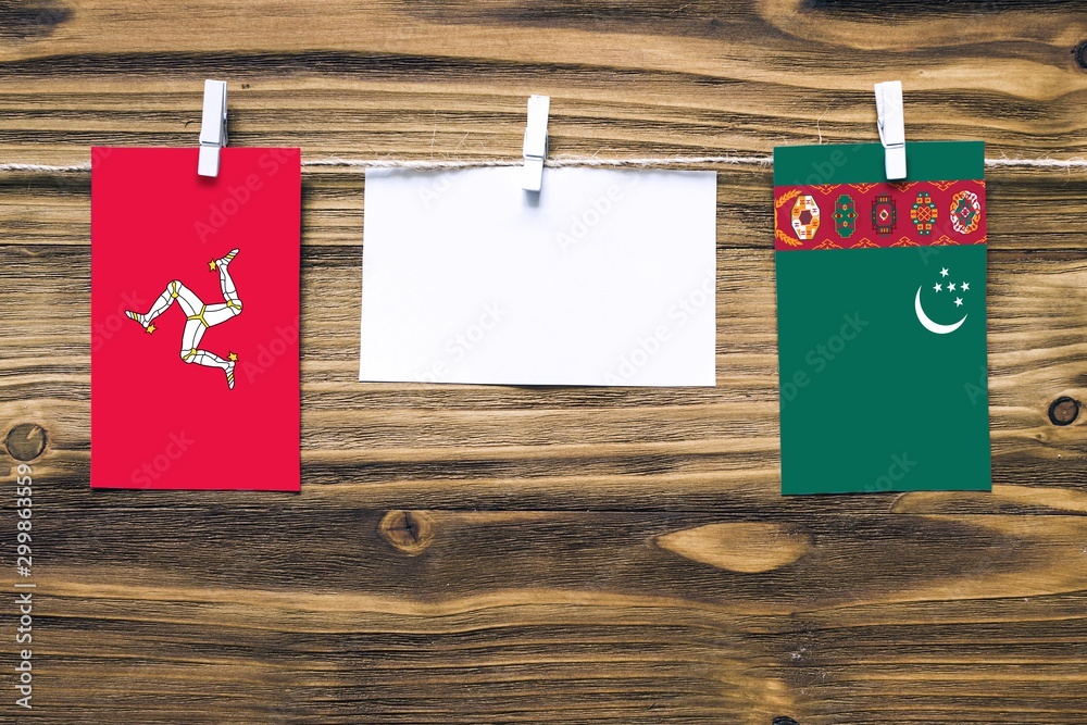 Wall mural Hanging flags of Isle Of Man and Turkmenistan attached to rope with clothes pins with copy space on white note paper on wooden background.Diplomatic relations between countries. - Wall murals