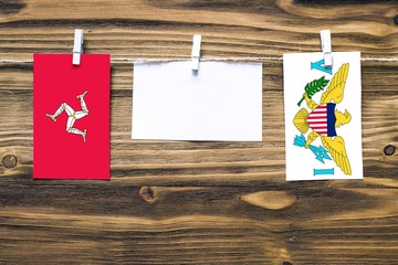 Hanging flags of Isle Of Man and United States Virgin Islands attached to rope with clothes pins with copy space on white note paper on wooden background.Diplomatic relations between countries.