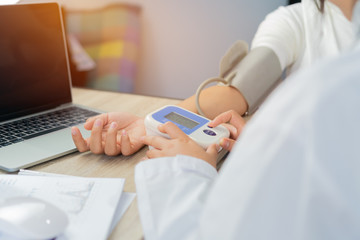 Doctor measuring blood pressure of young girl patient with pressure device monitor, in desk laptop computer consultation with gown stethoscope in clinic hospital, Healthcare medicine concept