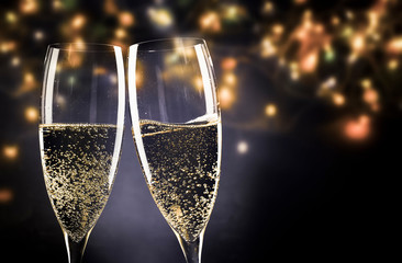 two champagne glasses ready to bring in the New Year - holiday lights and fireworks in the background
