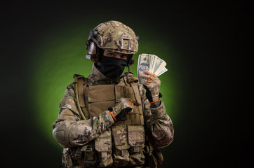 Fototapeta premium a male soldier in military clothes with a weapon on a dark background with money