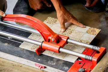 Closeup hands of laborer using cutting tile machine at construction site with sun flare background.