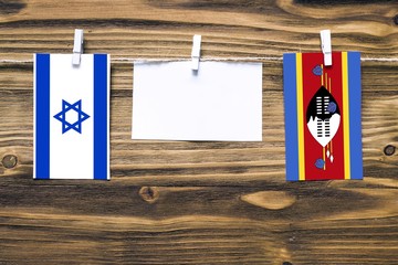 Hanging flags of Israel and Swaziland attached to rope with clothes pins with copy space on white note paper on wooden background.Diplomatic relations between countries.