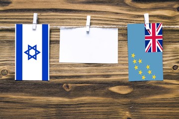 Hanging flags of Israel and Tuvalu attached to rope with clothes pins with copy space on white note paper on wooden background.Diplomatic relations between countries.