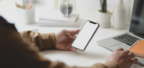 Cropped shot of young male freelancer holding blank screen smartphone