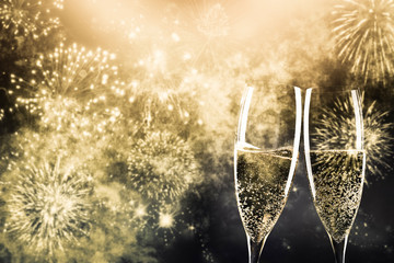 two champagne glasses ready to bring in the New Year - holiday lights and fireworks in the background
