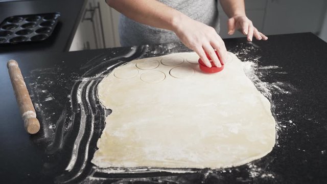 Woman Using A Tool To Cut Circle Shapes Into Dough Rolled Out In Flour On A Black Countertop. Lady Making Mince Pie Working On The Pastry Shell.