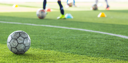Football on green artificial turf with blurry soccer team training. Blurry kid soccer player jogging between marker cones and control ball with soccer equipment in soccer academy.