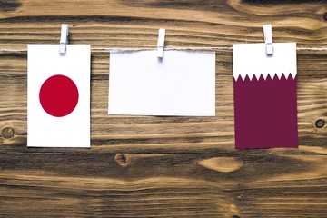 Hanging flags of Japan and Qatar attached to rope with clothes pins with copy space on white note paper on wooden background.Diplomatic relations between countries.