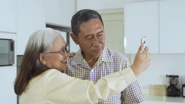 Happy elderly couple taking selfie photo together with a mobile phone while standing at home. Shot in 4k resolution