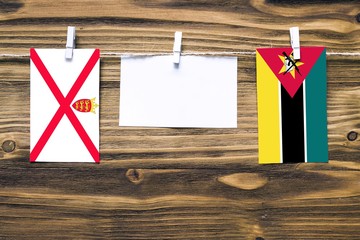 Hanging flags of Jersey and Mozambique attached to rope with clothes pins with copy space on white...