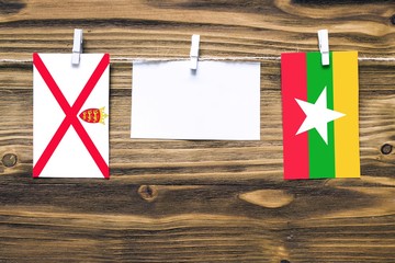 Hanging flags of Jersey and Myanmar attached to rope with clothes pins with copy space on white...