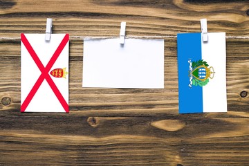 Hanging flags of Jersey and San Marino attached to rope with clothes pins with copy space on white...