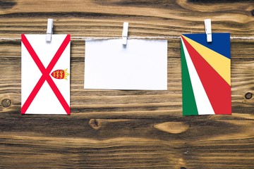 Fototapeta na wymiar Hanging flags of Jersey and Seychelles attached to rope with clothes pins with copy space on white note paper on wooden background.Diplomatic relations between countries.