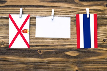 Hanging flags of Jersey and Thailand attached to rope with clothes pins with copy space on white...
