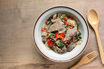 top view of stir fried beef with basil in a ceramic dish on wooden table. hot and spicy thai style food menu.