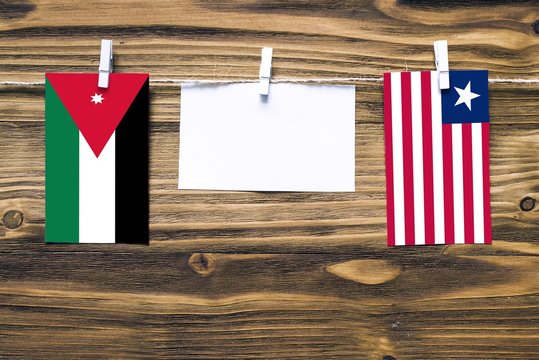 Hanging flags of Jordan and Liberia attached to rope with clothes pins with copy space on white note paper on wooden background.Diplomatic relations between countries.