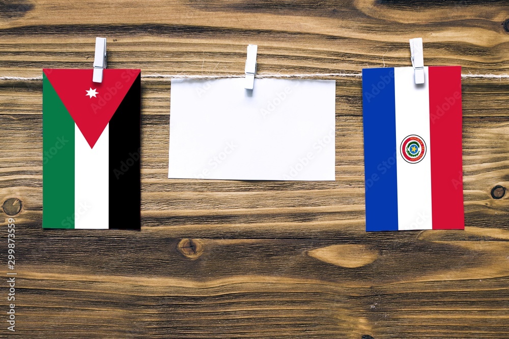 Wall mural Hanging flags of Jordan and Paraguay attached to rope with clothes pins with copy space on white note paper on wooden background.Diplomatic relations between countries. - Wall murals