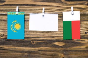 Hanging flags of Kazakhstan and Madagascar attached to rope with clothes pins with copy space on white note paper on wooden background.Diplomatic relations between countries.