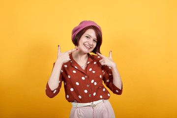 Girl wearing red shirt in white polka dot over isolated yellow background smiling confident showing and pointing with fingers teeth, mouth. Health concept. Looks funny, happy, nice.