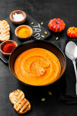 Pumpkin and carrot soup with spices on black background. 