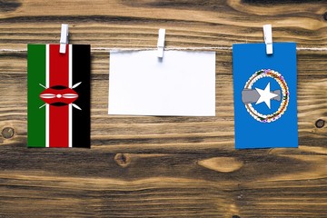 Hanging flags of Kenya and Northern Mariana Islands attached to rope with clothes pins with copy space on white note paper on wooden background.Diplomatic relations between countries.