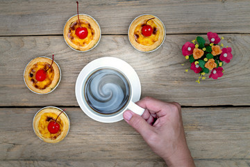 hand holding coffee cup with egg tart on wood table,top view
