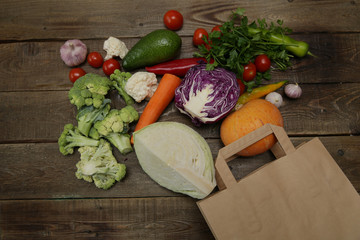 Organic fresh vegetables in a paper bag on a wooden background: Broccoli, carrots, avocado, tomatoes, garlic, cauliflower, cabbage, parsley, pepper, pumpkin. Healthy food concept. Vegan. Copy space