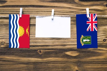 Hanging flags of Kiribati and British Virgin Islands attached to rope with clothes pins with copy space on white note paper on wooden background.Diplomatic relations between countries.