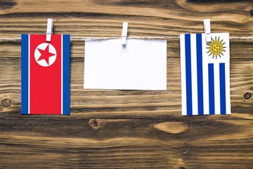 Hanging flags of North Korea and Uruguay attached to rope with clothes pins with copy space on white note paper on wooden background.Diplomatic relations between countries.