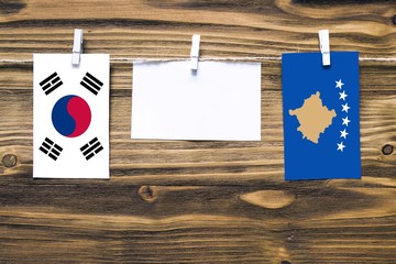 Hanging flags of South Korea and Kosovo attached to rope with clothes pins with copy space on white note paper on wooden background.Diplomatic relations between countries.