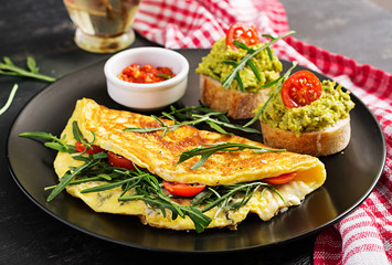 Breakfast. Omelette with tomatoes, cheese, green arugula and toasts with avocado cream on black plate. Frittata - italian omelet.