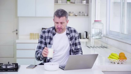 Caucasian man working with laptop and spill a glass of milk accidentally on the laptop in the kitchen at home. Shot in 4k resolution