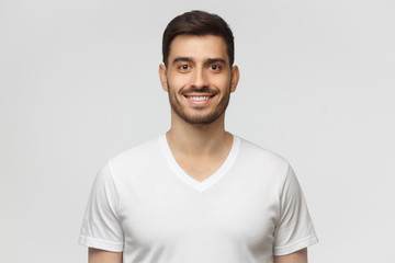 Portrait of smiling handsome young man in white t-shirt, looking at camera, isolated on gray background - obrazy, fototapety, plakaty