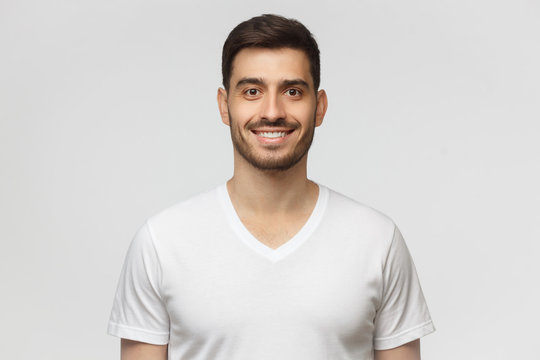 Portrait of smiling handsome young man in white t-shirt, looking at camera, isolated on gray background