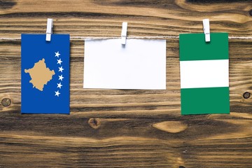 Hanging flags of Kosovo and Nigeria attached to rope with clothes pins with copy space on white note paper on wooden background.Diplomatic relations between countries.