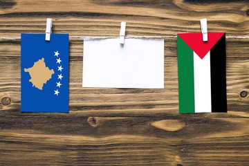 Hanging flags of Kosovo and Palestine attached to rope with clothes pins with copy space on white note paper on wooden background.Diplomatic relations between countries.