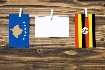 Hanging flags of Kosovo and Uganda attached to rope with clothes pins with copy space on white note paper on wooden background.Diplomatic relations between countries.