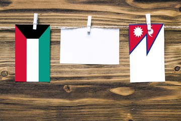 Hanging flags of Kuwait and Nepal attached to rope with clothes pins with copy space on white note paper on wooden background.Diplomatic relations between countries.