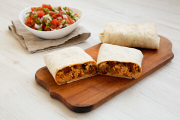 Homemade chorizo breakfast burritos on a rustic wooden board on a white wooden background, side view.