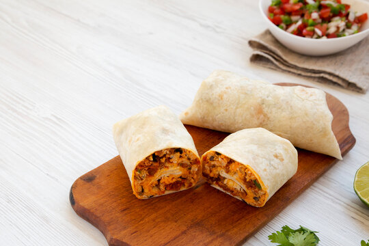 Homemade chorizo breakfast burritos on a rustic wooden board on a white wooden surface, side view. Copy space.