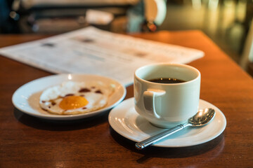 Black coffee on the table with fried egg and business newspaper.