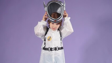 Little astronaut kid boy wearing white protective suit and helmet stand isolated over purple background, look at camera - Powered by Adobe