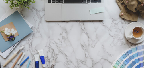 Overhead shot of light blue feminine designer workspace with laptop computer and painting tools on...