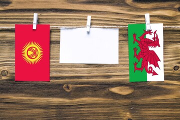 Hanging flags of Kyrgyzstan and Wales attached to rope with clothes pins with copy space on white...