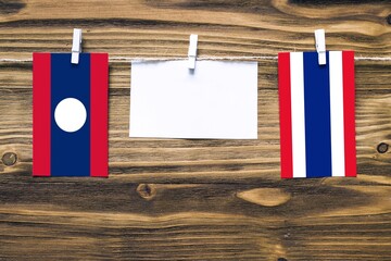 Hanging flags of Laos and Thailand attached to rope with clothes pins with copy space on white note...