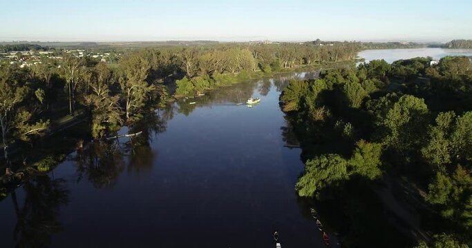 Aerial drone scene of fishing boat sailing along riverbend at foggy morning. Flying over water following boat from panoramic view of landscape to top view of ship. Rio Negro, Mercedes, Uruguay