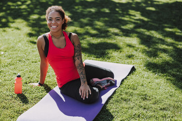 Joyful young woman sitting on yoga mat outdoors