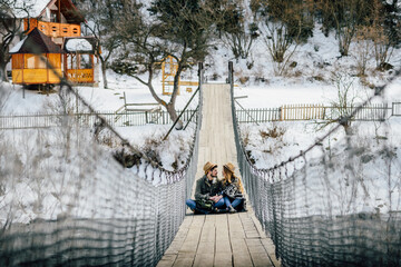 Loving couple of travelers on suspension bridge in winter in mountains.
