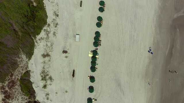 Aerial: Drone moving over people relaxing under parasols at beach on sunny day during summer weekend - Kiawah Island, SC